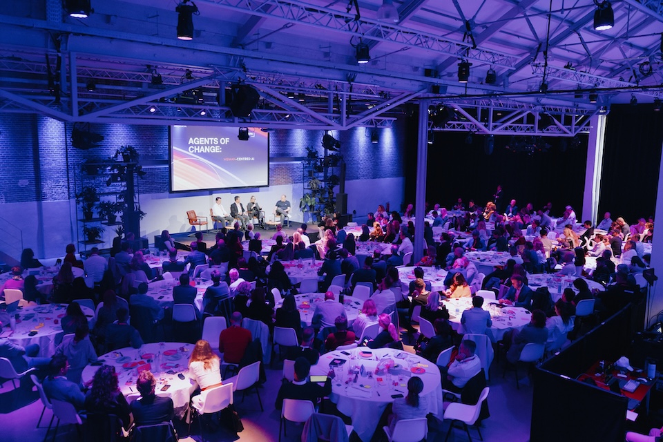 A room of people, looking at a group f people on stage